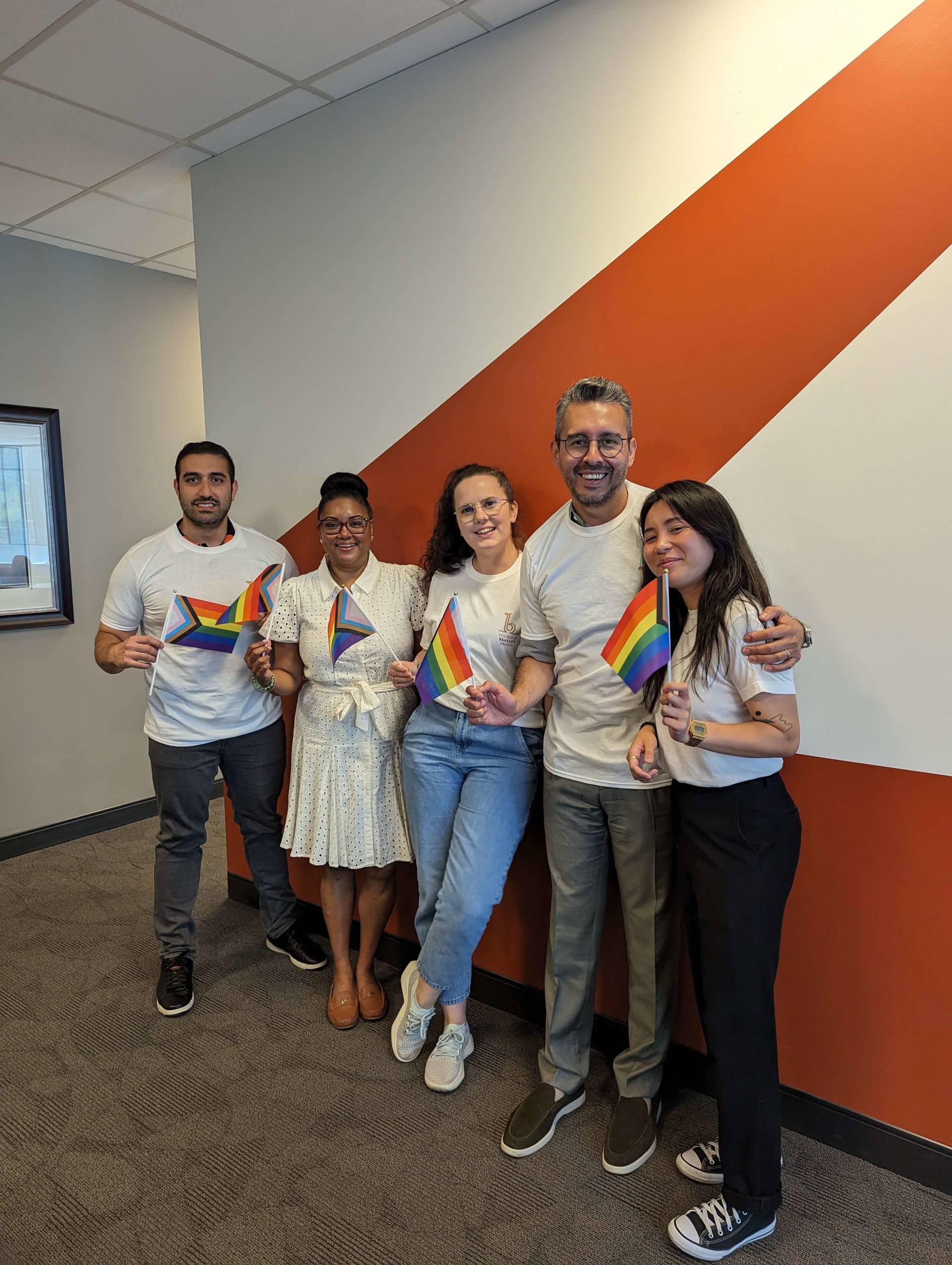 A team of proud colleagues standing together, smiling for a group photo in a well-lit office environment.