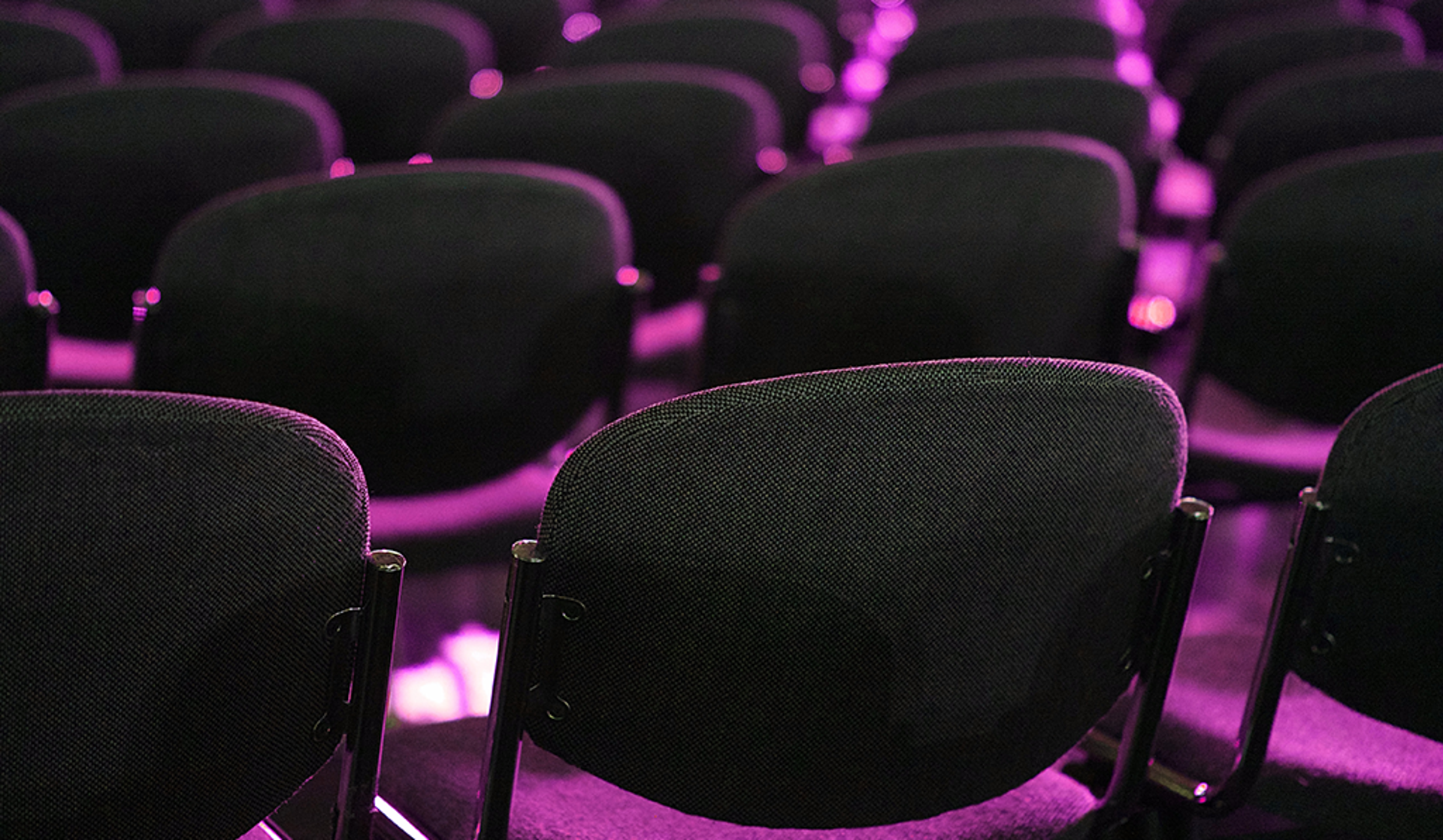 A series of chairs positioned in a darkened event space, evoking a sense of stillness and solitude.