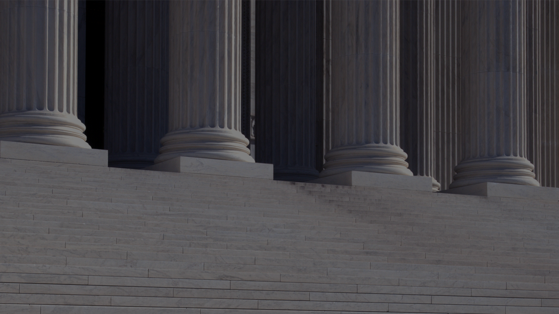 A man walks down the steps of a neo-classical building, surrounded by impressive columns that define its architectural style.