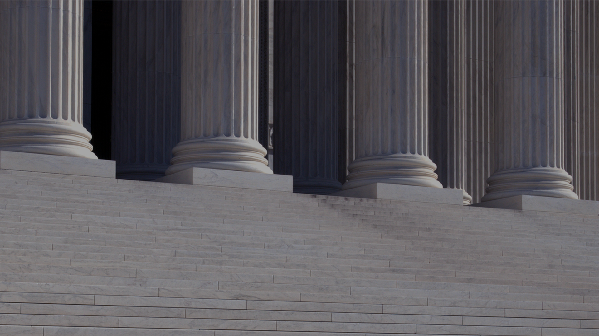 A man walks down the steps of a neo-classical building, surrounded by impressive columns that define its architectural style.
