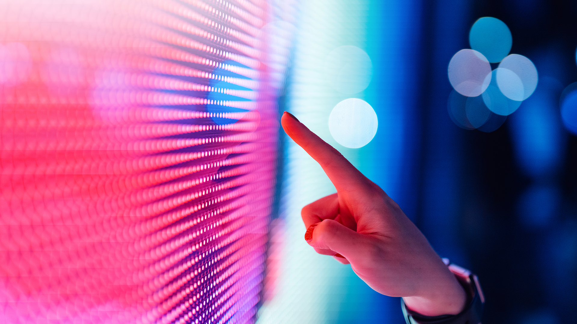 A person gestures towards a vibrant, colorful screen, highlighting its dynamic visual display.