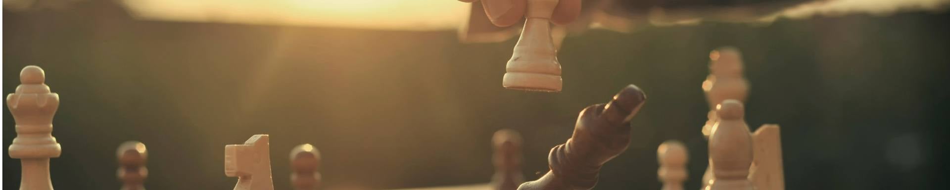 An individual playing chess, strategically positioning wooden pieces on a traditional chessboard, against the backdrop of a warm sunset.